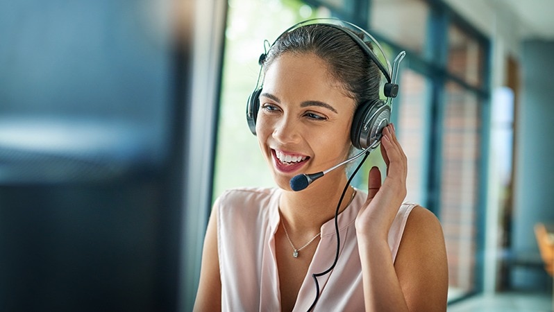 Frau mit Headset lächelt und berät telefonisch.