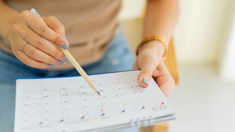 Hände mit Kalender und Bleistift für Terminplanung.