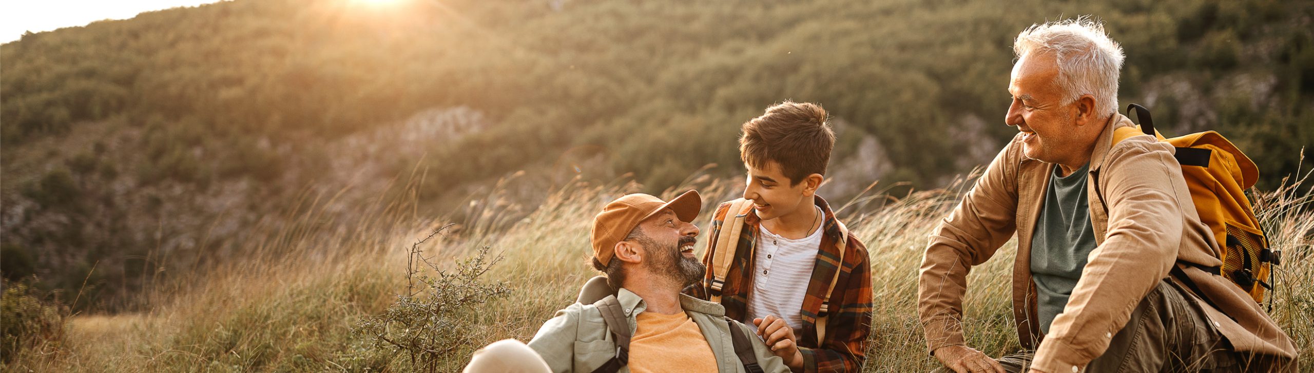 Drei Generationen Männer sitzen lachend beim Wandern.