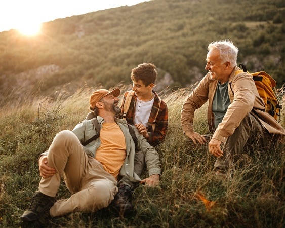 Drei Generationen Männer sitzen lachend beim Wandern.