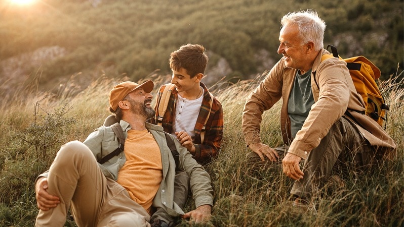 Drei Generationen Männer sitzen lachend beim Wandern.