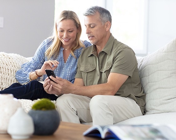 Paar sitzt auf einem Sofa und schaut gemeinsam auf ein Smartphone.