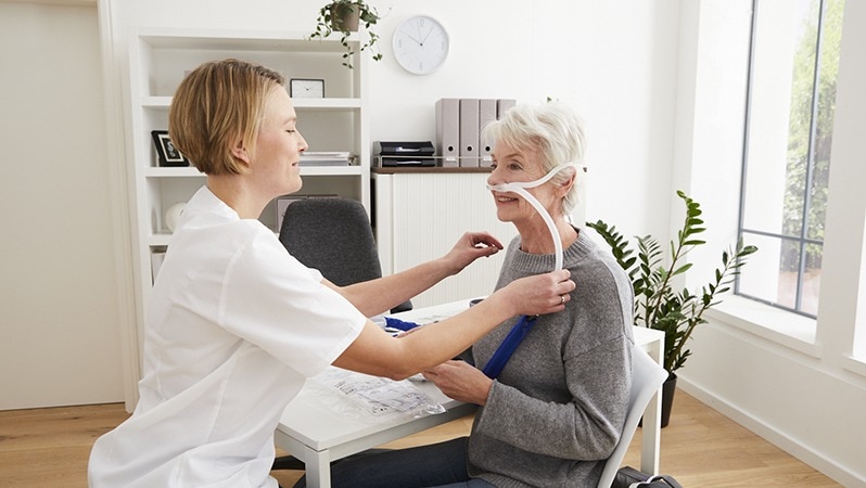 Eine medizinische Fachkraft passt einer älteren Frau eine Atemmaske für die Therapie an.