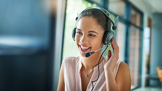 Frau mit Headset lächelt und berät telefonisch.